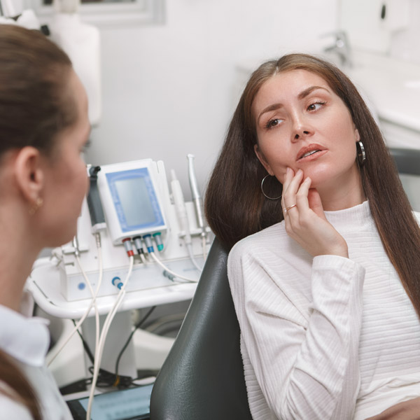 woman touching the side of her face while talking with a dentist